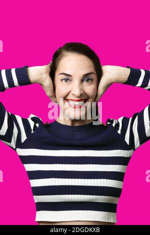 Lustige Frau, die ihre Ohren bedeckt und Kamera mit toothy Lächeln, glücklich, fröhlich über lila. Stockfoto