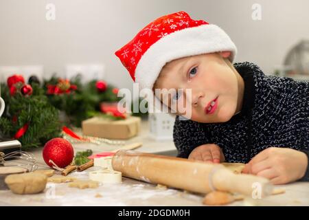 Boy 7-10 in einer Weihnachtsmütze, die Weihnachts-Lebkuchenkekse in der Neujahrsküche macht. Stockfoto