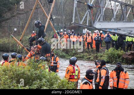 Denham, Großbritannien. Dezember 2020. Gerichtsvollzieher übergeben Dan Hooper, der in den 1990er Jahren als Swampy bekannt war, an Hampshire Polizeibeamte, nachdem er ihn von einem Bambusstativ im Fluss Colne entfernt hatte. Der Klima- und Straßenaktivist hatte am Vortag das Stativ besetzt, um den Bau einer Brücke im Rahmen der Arbeiten für die umstrittene Hochgeschwindigkeits-Eisenbahnverbindung HS2 und eine große Sicherheitsoperation mit Beamten von mindestens drei Polizeikräften zu verzögern, Das Nationale Räumungsteam und die Sicherheitskräfte des HS2 wurden eingesetzt, um seine Entfernung zu erleichtern. Kredit: Mark Kerrison/Alamy Live Ne Stockfoto