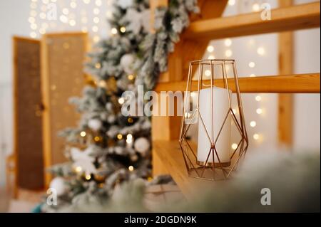 Kerzenständer aus Metall Gold im Loft-Stil mit hoher weißer Kerze im Inneren Auf Holztreppe in einer Wohnung für Weihnachten mit dekoriert Weihnachtsbäume und g Stockfoto