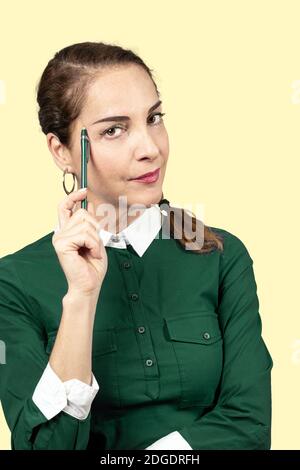 Porträt einer Frau, die die Kamera mit einem Stift in einem grünen Hemd auf dem Tempel hält. Stockfoto