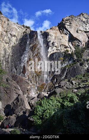 Besucher klettern über die Felsbrocken, um einen näheren Blick auf Bridal Veil Falls im Yosemite National Park, Kalifornien, zu bekommen. Große Granitklippe und Wasserfall. Stockfoto