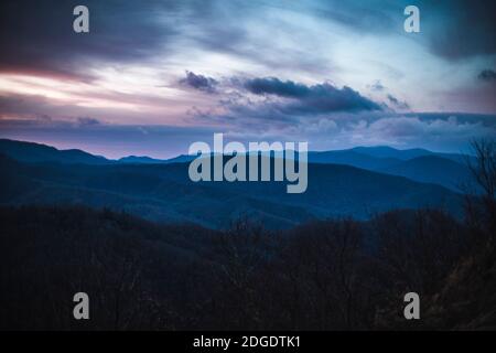 Dramatische rosa und lila Wolken über rauchigen Bergen bei Sonnenaufgang Stockfoto