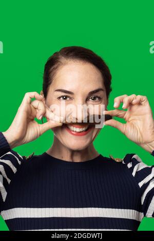 Lustige Frau macht einen Schnurrbart mit ihren Haaren mit toothy Lächeln glücklich, über grünem Hintergrund Stockfoto