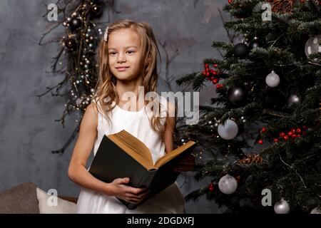 Happy Kind Eröffnung Weihnachtsbuch. Weihnachtsfeiertagskonzept. Mädchen lesen ein Buch in dekorierten Wohnzimmer mit Weihnachtsbaum Stockfoto