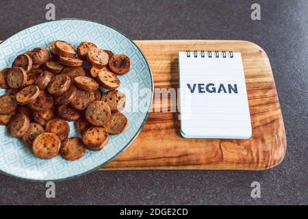 Gesunde pflanzliche Rezeptur Konzept, vegane Wurst in Salami-Scheiben geschnitten und Pfanne gebraten mit gerissenem Pfeffer auf der Oberseite neben Memo mit Vegan writte Stockfoto