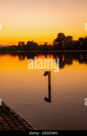 Warmes rot orange gelbes Feuer lebhafter Sonnenuntergang über dem Ruderkanal Ruhige Wasser- und Baumsilhouetten kopieren Platz für Text Stockfoto