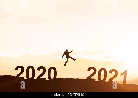 Silhouette eines Geschäftsmannes, der von 2020 bis 2021 mit einem Sonnenuntergangshintergrund springt. Frohes Neues Jahr 2021 Stockfoto