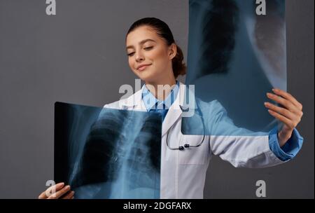 Eine Frau in einem medizinischen Kleid untersucht Röntgenstrahlen auf einem Grauer Hintergrund Stockfoto