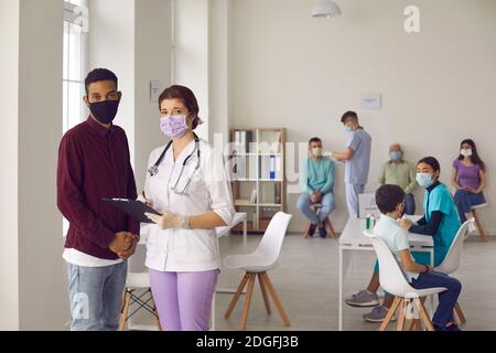 Krankenschwester und Patient in Gesichtsmasken stehen im Krankenhausbüro Während der Impfkampagne Stockfoto