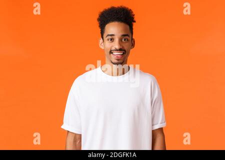 Fröhlicher junger Hipster afroamerikanischer Kerl mit Schnurrbart und Afro-Haarschnitt, trägt weißes T-Shirt, lächelnd niedlich aussehende Kamera Stockfoto