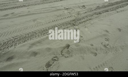 Fußspuren, die Reifenabdrücke im Sand am Waitarere Beach, NZ kreuzen Stockfoto