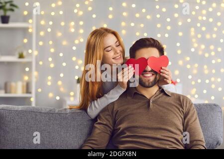 Frau, die die Augen des Freundes mit roten herzförmigen Karten auf Saint bedeckt Valentinstag Stockfoto