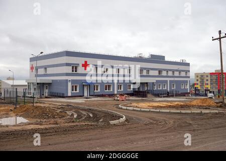 An einem bewölkten Herbsttag führt eine unbefestigte Straße zu einem städtischen Krankenhausgebäude, das an einem Projektstandort im Bau ist. Stockfoto