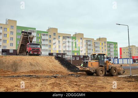 Ein großer Muldenkipper und ein Gabelstapler planen einen Platz vor einem neu errichteten Mehrfamilienhaus im Dorf Tayoschny, Region Krasnojarsk. Stockfoto