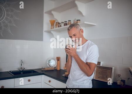 Grauhaariger großer Mann, der eine Tasse hält und nachdenklich aussieht Stockfoto