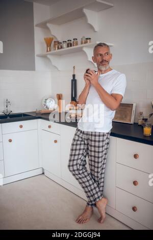 Grauhaariger großer Mann, der eine Tasse hält und nachdenklich aussieht Stockfoto