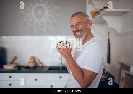 Grauhaariger großer Mann, der eine Tasse hält und freundlich lächelt Stockfoto