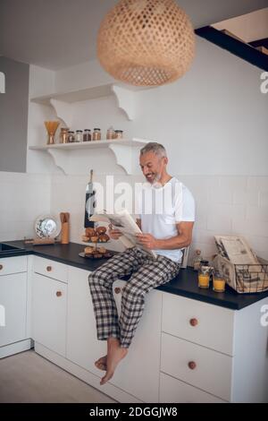 Grauhaariger großer Mann, der in der Küche eine Zeitung liest Stockfoto