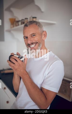 Grauhaariger großer Mann, der eine Tasse hält und freundlich lächelt Stockfoto