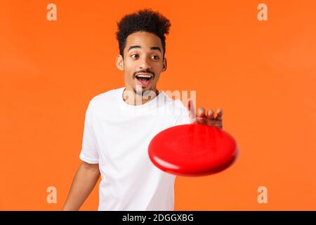 Sorglos freundlich und glücklich lächelnd jungen modernen afroamerikanischen Mann in weißem T-Shirt, Fang Frisbee und im Gespräch mit Mate, Th Stockfoto