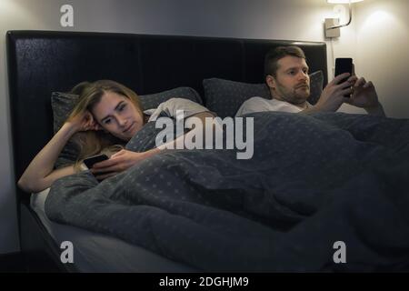 Verheiratetes Paar mit Smartphones im Bett ignorieren einander. Relationship Routine Kommunikation Probleme Internet sucht Konzept Stockfoto