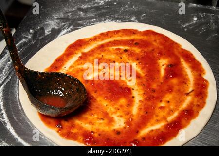 Hinzufügen von Tomatensauce während der Zubereitung der italienischen Pizza Stockfoto
