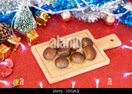 Weihnachtsschmuck und Kastanien auf Holzbrett für die Präsentation von Lebensmitteln Stockfoto
