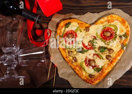 Pizza in Form eines Herzens und Wein mit Gläser auf dunklem Holzhintergrund Stockfoto