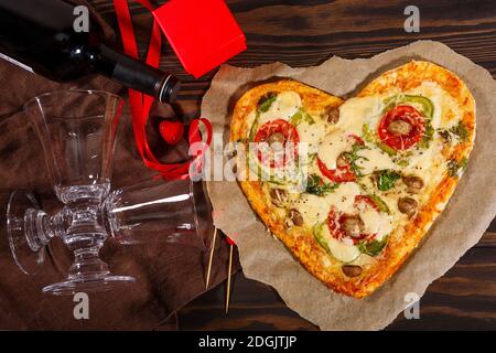 Pizza in Form eines Herzens und Wein mit Gläser auf dunklem Holzhintergrund Stockfoto