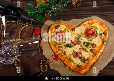 Pizza in Herzform, eine Flasche Wein und Weihnachtsschmuck Stockfoto