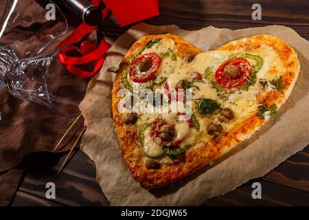 Pizza in Form eines Herzens und Wein mit Gläser auf dunklem Holzhintergrund Stockfoto