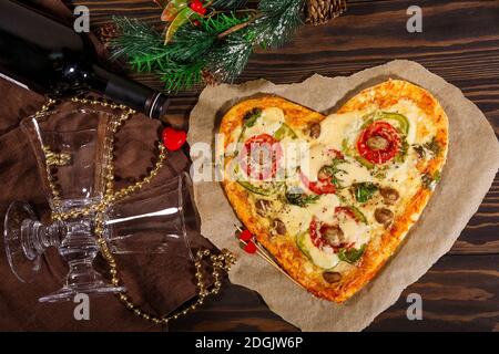 Pizza in Herzform, eine Flasche Wein und Weihnachtsschmuck Stockfoto