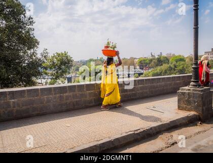 PUNE, INDIEN - 14. MÄRZ 2019: Frau in gelber Nationaltracht Saree trägt auf ihrem Kopf ein Becken mit Blumentöpfen in Pune, Indien Stockfoto