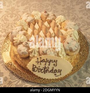 Saint Honore Kuchen garniert mit Sahne Puffs und einer Schokolade Teller mit den Worten Happy Birthday Stockfoto