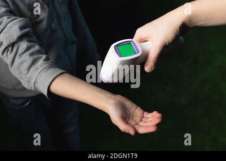 Messung der Temperatur am Handgelenk des Kindes mit berührungsloser Infrarot-Funktion Thermometer Pistole auf dunklem Hintergrund Stockfoto