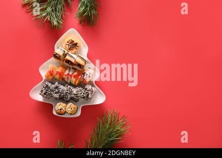 Sushi-Set in Teller als Weihnachtsbaum verzierten Tannenzweigen auf rotem Hintergrund. Blick von oben. Leerzeichen für Text. Flatlay-Style. Stockfoto