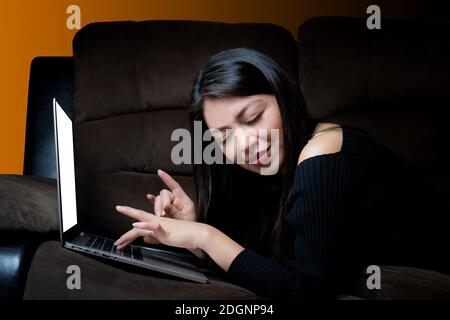 Junge Frau lächelt vor dem Computer, auf dem sie ruht Ein Sofa Stockfoto