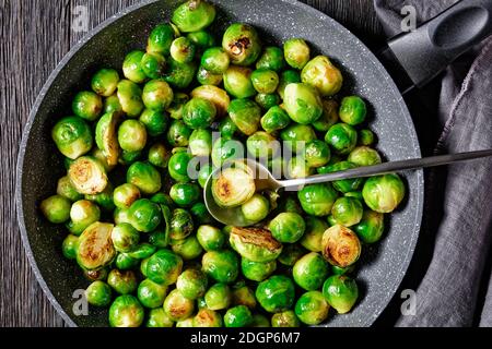 Rosenkohl mit Knoblauch gebraten und auf einer Pfanne auf dunklem Holzboden mit Leinentuch serviert, Nahaufnahme, Draufsicht Stockfoto