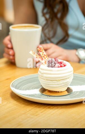 Süßer weißer Cupcake mit Beeren auf dem Teller am Tisch auf dem Hintergrund einer Frau mit einer Tasse Kaffee In einem Café Stockfoto
