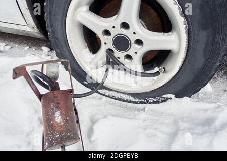 Reifenpanne auf einem Auto im Winter. Alte Fußpumpe bläst das Rad auf Stockfoto