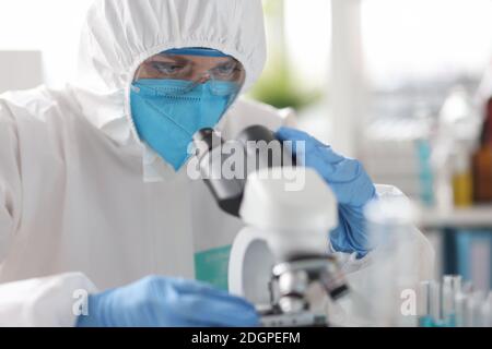 Wissenschaftler in Schutzanzug und Atemschutzmaske Blick durch Mikroskop in Labor Stockfoto