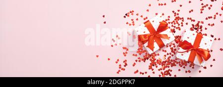 Weiße Geschenkschachteln mit roter Schleife und rotem Herzkonfetti auf pastellrosa Hintergrund. Valentinstag Banner mit Geschenken. Muttertag präsent, b Stockfoto