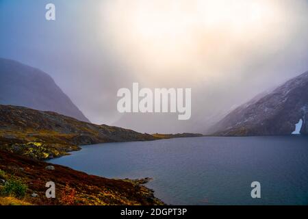 Dramatische Sturmwolken mit hellem Sonnenlicht, das durchbricht. Hochplateau mit einem klaren blauen See. Stockfoto