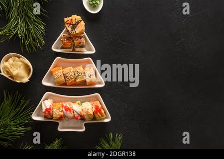 Sushi-Set serviert auf dem Teller als Weihnachtsbaum mit Weihnachtsdekoration auf schwarzem Hintergrund. Blick von oben. Leerzeichen für Text. Flache Lay-Optik. Stockfoto