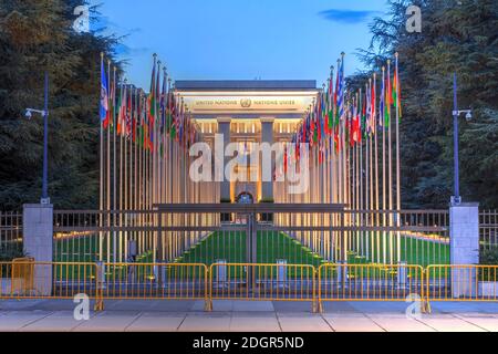 Büro der Vereinten Nationen von Genf (UNOG), Schweiz bei Nacht, mit dem Haupteingang A die Fahnenmasten der Mitgliedsstaaten. Stockfoto