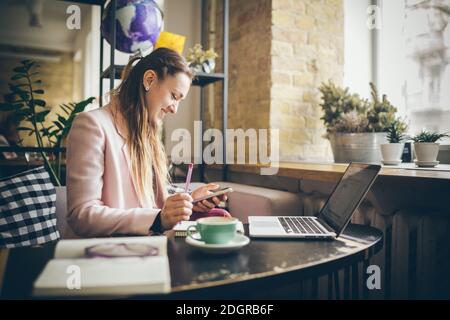 Erfolgreiches Geschäft. Auslagern. Bloggerin sitzt im Café und nutzt Smartphone, prüft E-Mail, kommuniziert mit Followern, liest ne Stockfoto