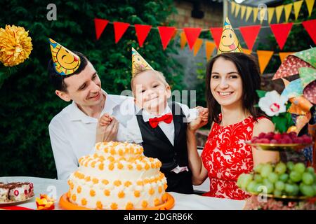 Geburtstagsthema für Kinder: Familie von drei Kaukasiern, die im Hinterhof des Hauses an einem festlich dekorierten Tisch in lustiger Stimmung sitzen Stockfoto