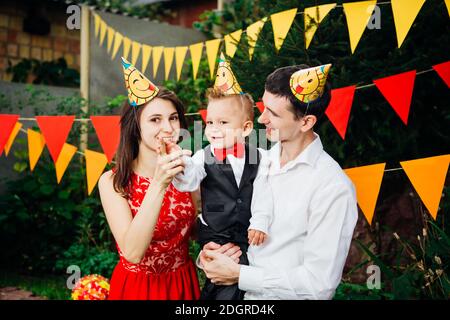 Thema Kinder Geburtstagsfeier. Familie Vater und Mutter Holding Sohn eines Jahres auf dem Hintergrund von Grün und festliche Einrichtung, Stockfoto