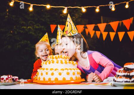 Kindergeburtstag. Drei fröhliche Kindermädchen am Tisch essen Kuchen mit den Händen und schmieren ihr Gesicht. Spaß Stockfoto